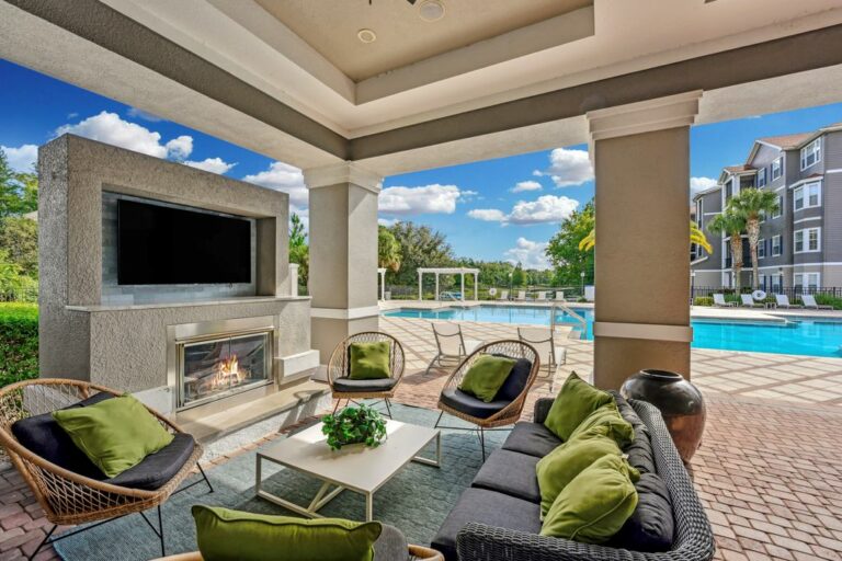 Luxurious outdoor lounge featuring a cozy fireplace, stylish seating, and a swimming pool view framed by lush greenery and elegant architecture.