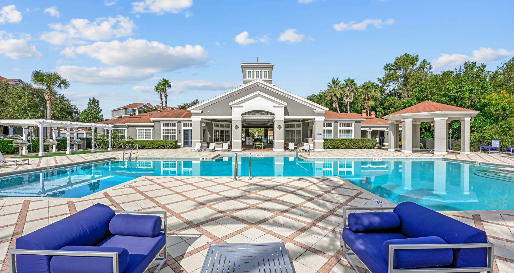 Swimminng pool area featuring stylish outdoor seating, large swimming pool, and elegant clubhouse under a bright blue sky.